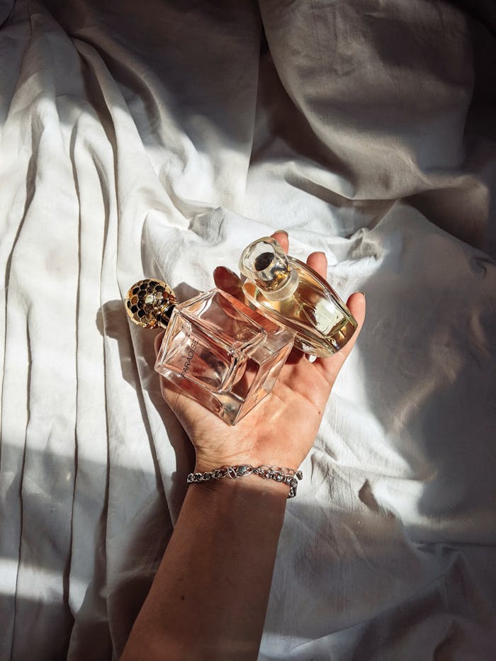 An elegant hand delicately holding luxury perfume bottles against a soft fabric background.