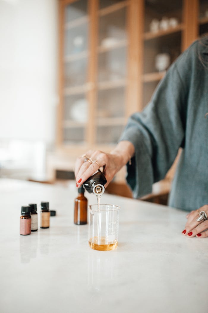 A woman in a cozy kitchen pouring essential oil into a beaker on the counter.